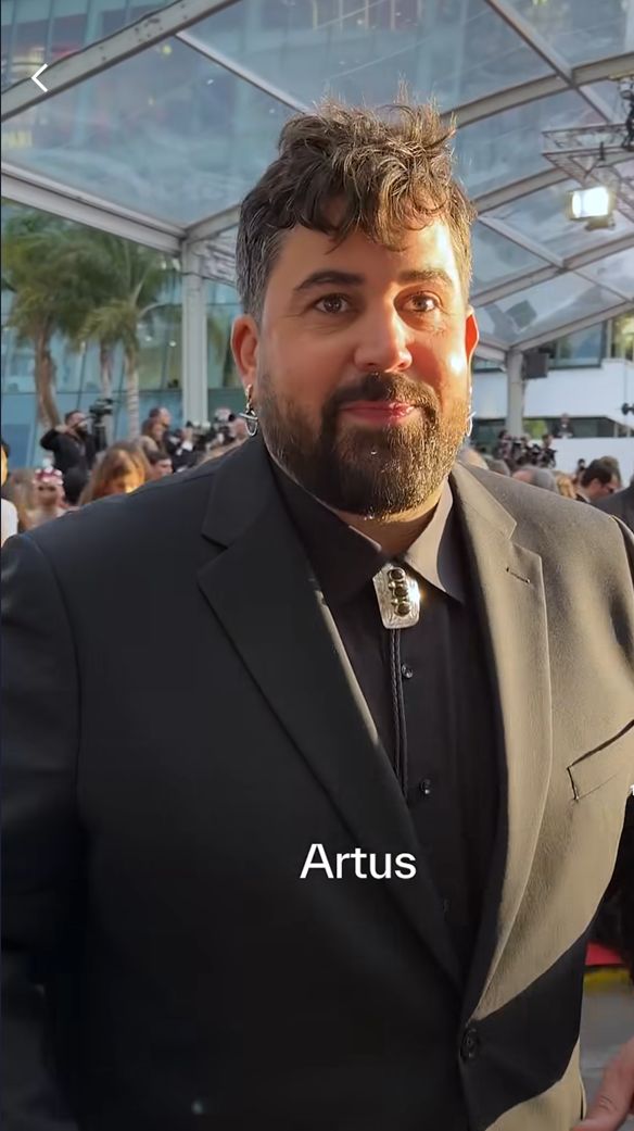 Artus — мужчина с подвеской на черном пиджаке