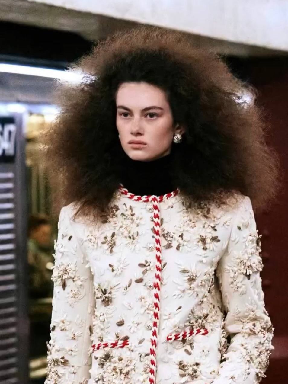 Chanel Métiers d'Art 2026 — модель с пышными кудрями в белом жакете с цветочным декором