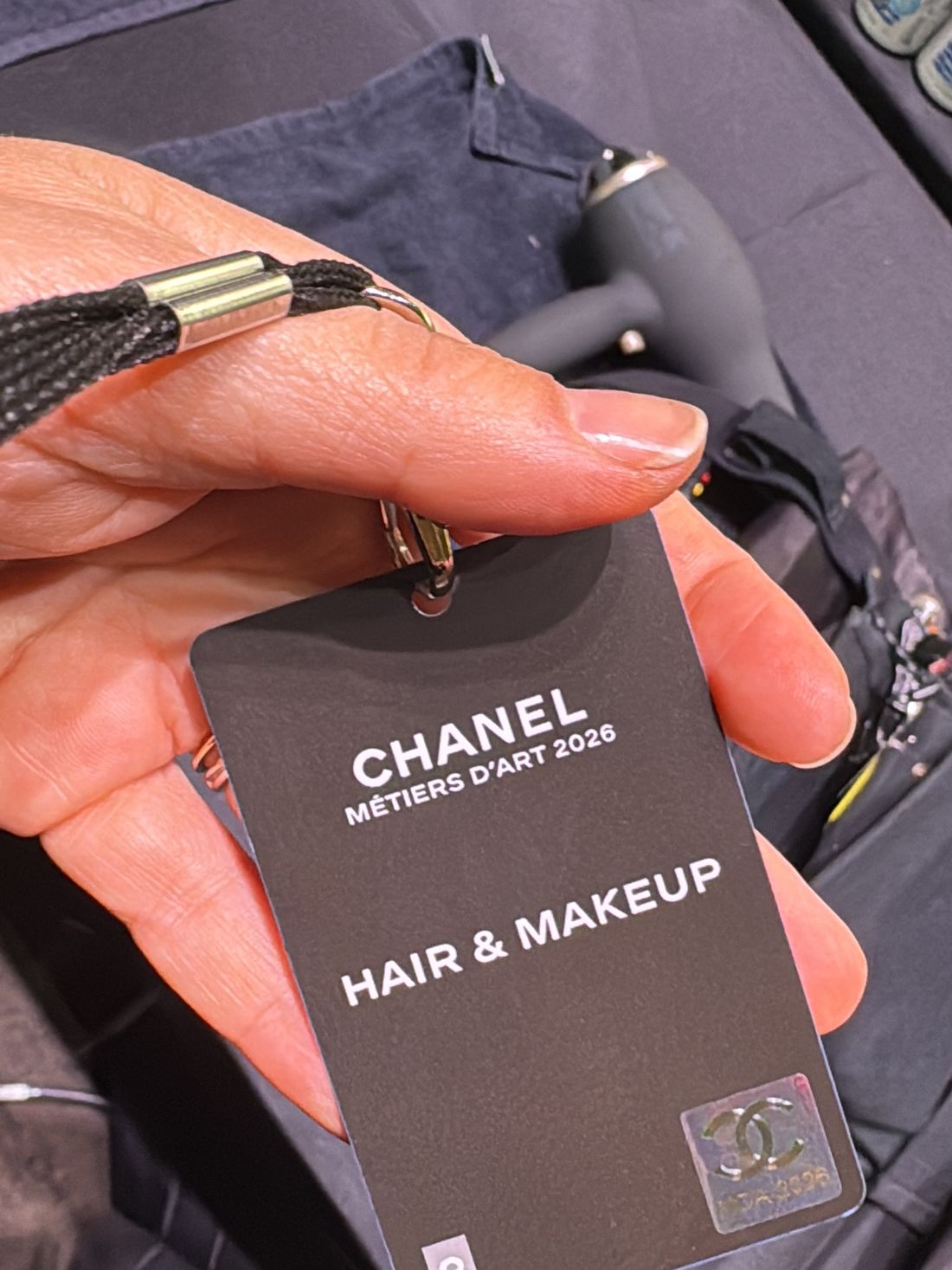 Бэкстейдж-пропуск Chanel Métiers d'Art 2026 HAIR & MAKEUP в руке
